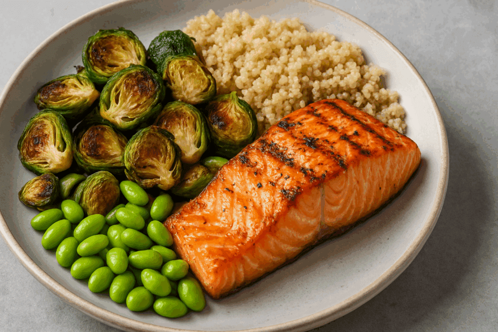 The Essential Guide to High Fiber Foods for Gut Health: How to Get More Fiber in Your Diet Naturally and Effectively 4 Grilled salmon with quinoa, roasted Brussels sprouts, and edamame on a plate—perfect for learning how to get more fiber in your diet.