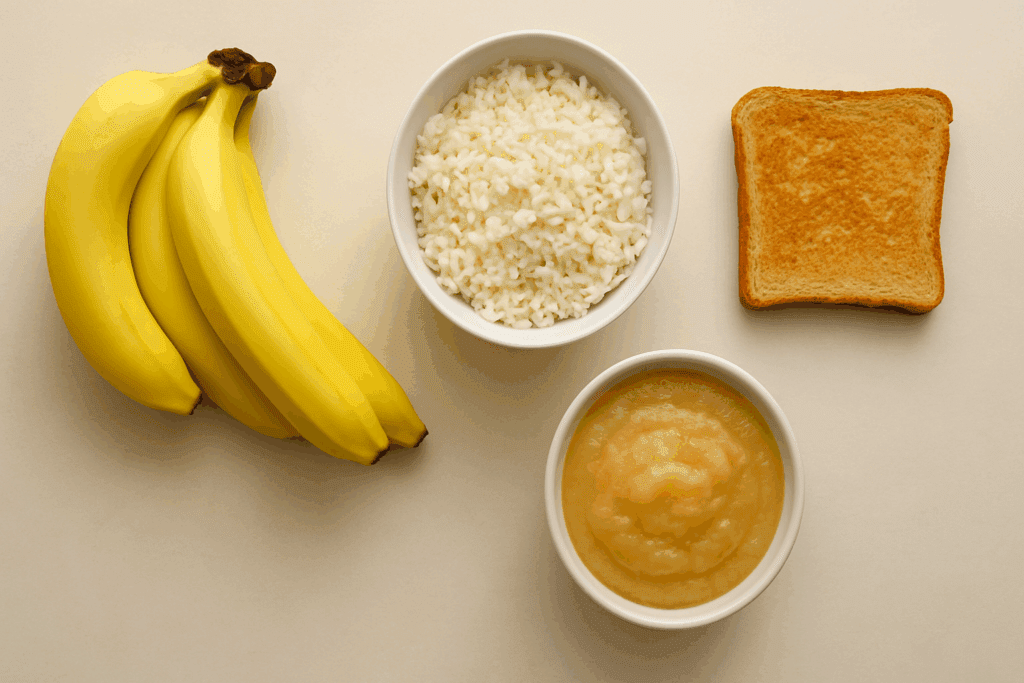 The Essential Guide to What to Eat When You Have Diarrhea: Proven Foods That Help Soothe and Settle an Upset Stomach 1 Flat-lay of bananas, white rice, applesauce, and toast on a beige background—classic examples of what to eat when you have diarrhea.